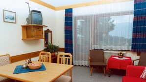 A small, cozy living room with a wooden dining table, two chairs, a red sofa, and a television on a wooden cabinet. - Apartments Home Hermann, Ramsau am Dachstein (Ramsau am Dachstein)