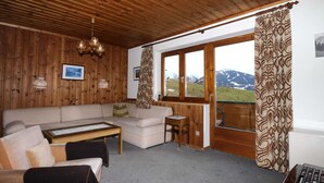 A cozy living room with a wooden ceiling, a sofa, a small table, and a view of mountains through a large window. - Apartments Home Hermann, Ramsau am Dachstein (Ramsau am Dachstein)