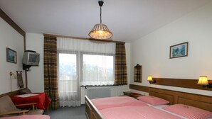 A hotel room with a bed, a desk, a chair, a television, and a window with curtains. - Apartments Home Hermann, Ramsau am Dachstein (Ramsau am Dachstein)