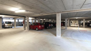 Un parking souterrain avec des piliers en béton, de nombreuses places de stationnement et quelques voitures garées.