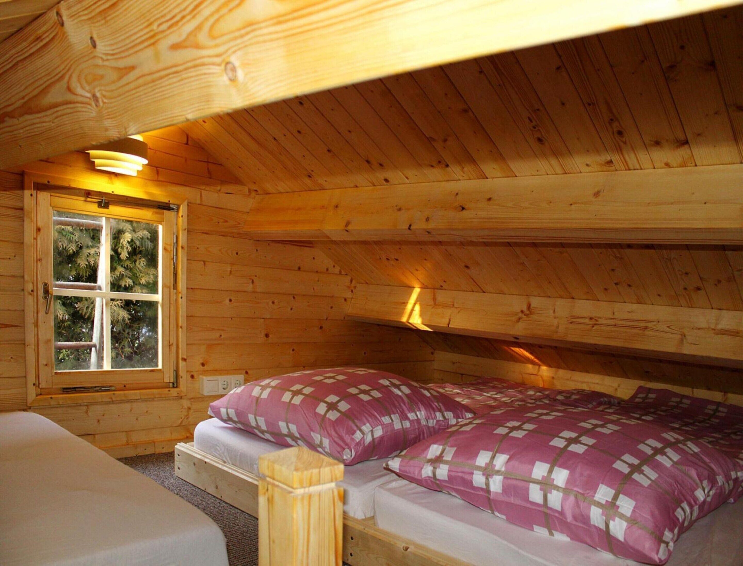 A wooden cabin room with a bed, a window, and a ceiling light.