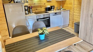 A compact kitchen with a stove, sink, and cabinets, a small dining table with a plant, and wooden walls. - Wunderschones Blockbohlenhaus am Plauer See (Plau am See)