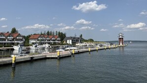 A marina with boats docked, a lighthouse, and residential buildings in the background. - Wunderschones Blockbohlenhaus am Plauer See (Plau am See)