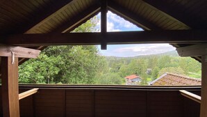 Una habitación con techo de madera inclinado y un ventanal grande con vistas a un valle boscoso y una casa.