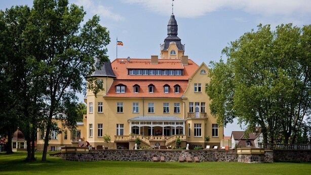 A large, yellow building with a red-tiled roof, a prominent tower, and a flag. - Reihenhaus Reiterchalet in Wendorf (Kuhlen-Wendorf)
