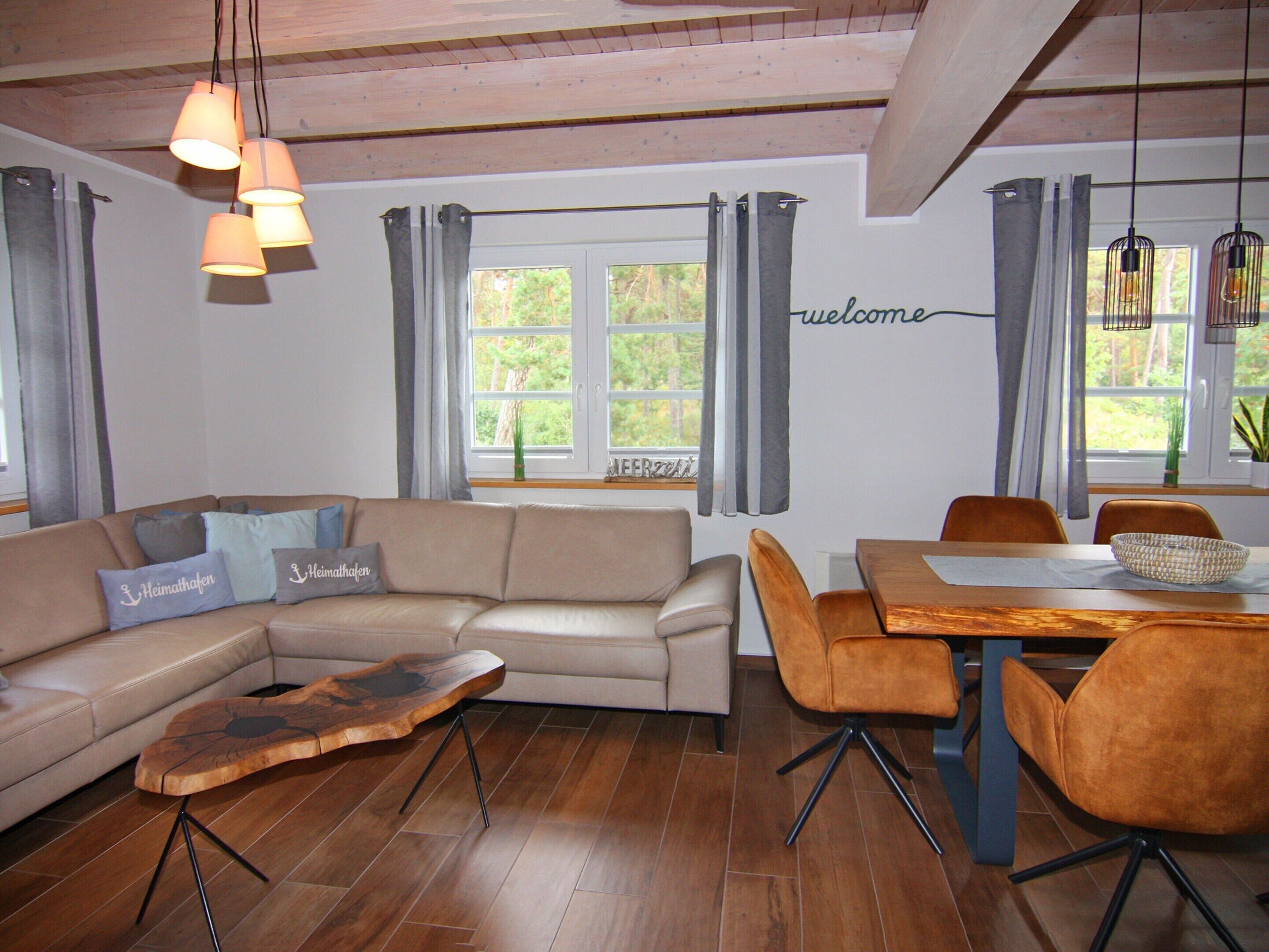 Una sala de estar moderna con un sofá modular, una mesa de centro de madera, una mesa de comedor con sillas y un cartel con la palabra 'welcome' en la pared.