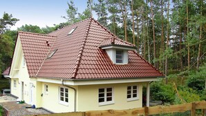 A house with a red-tiled roof, a small attic window, and a wooden fence in front. - Doppelhaushalfte Dunenhaus I, Trassenheide (Trassenheide)