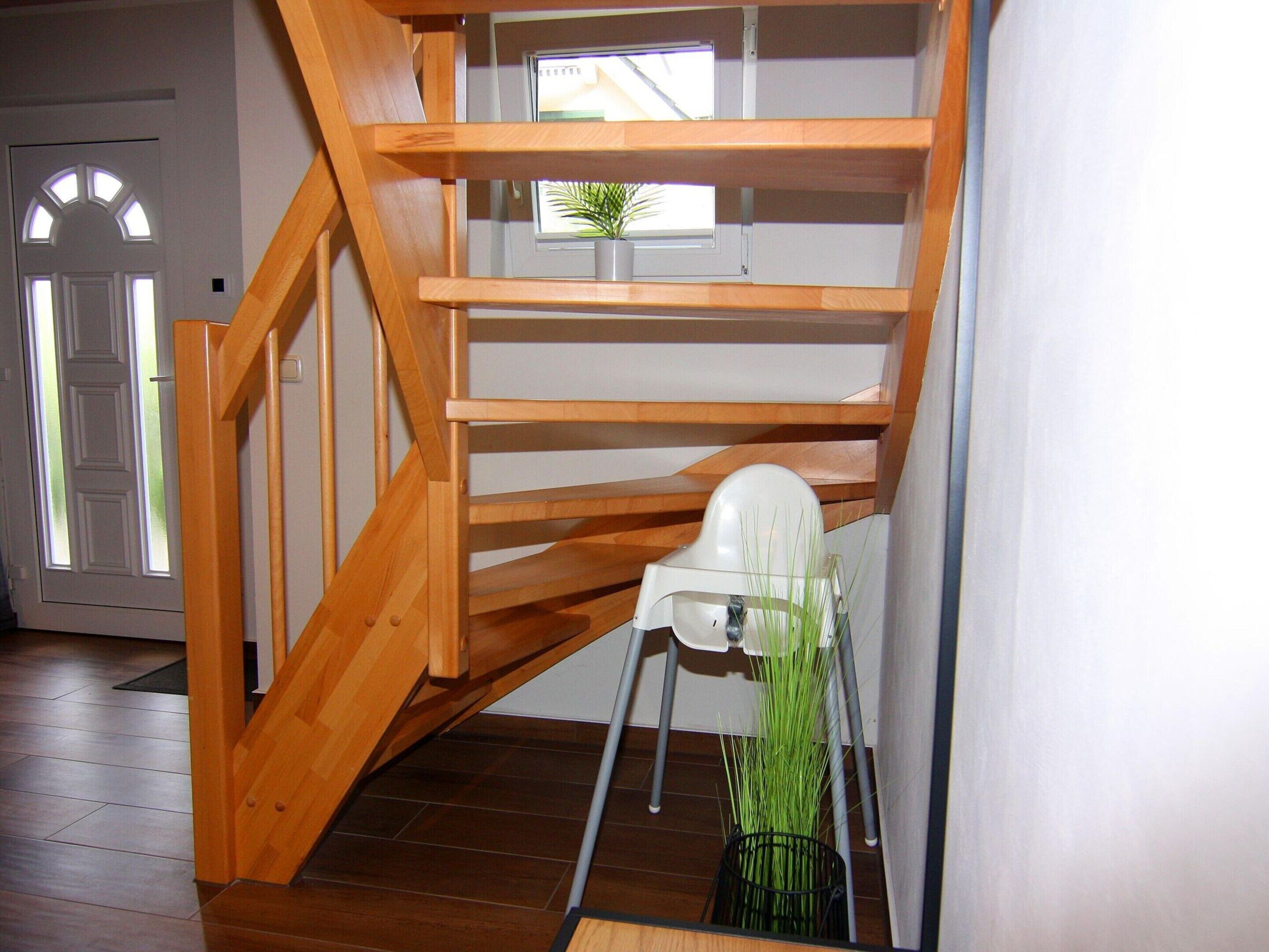 Eine Holztreppe mit einem weißen Stuhl und einem Blumentopf am Fuß.