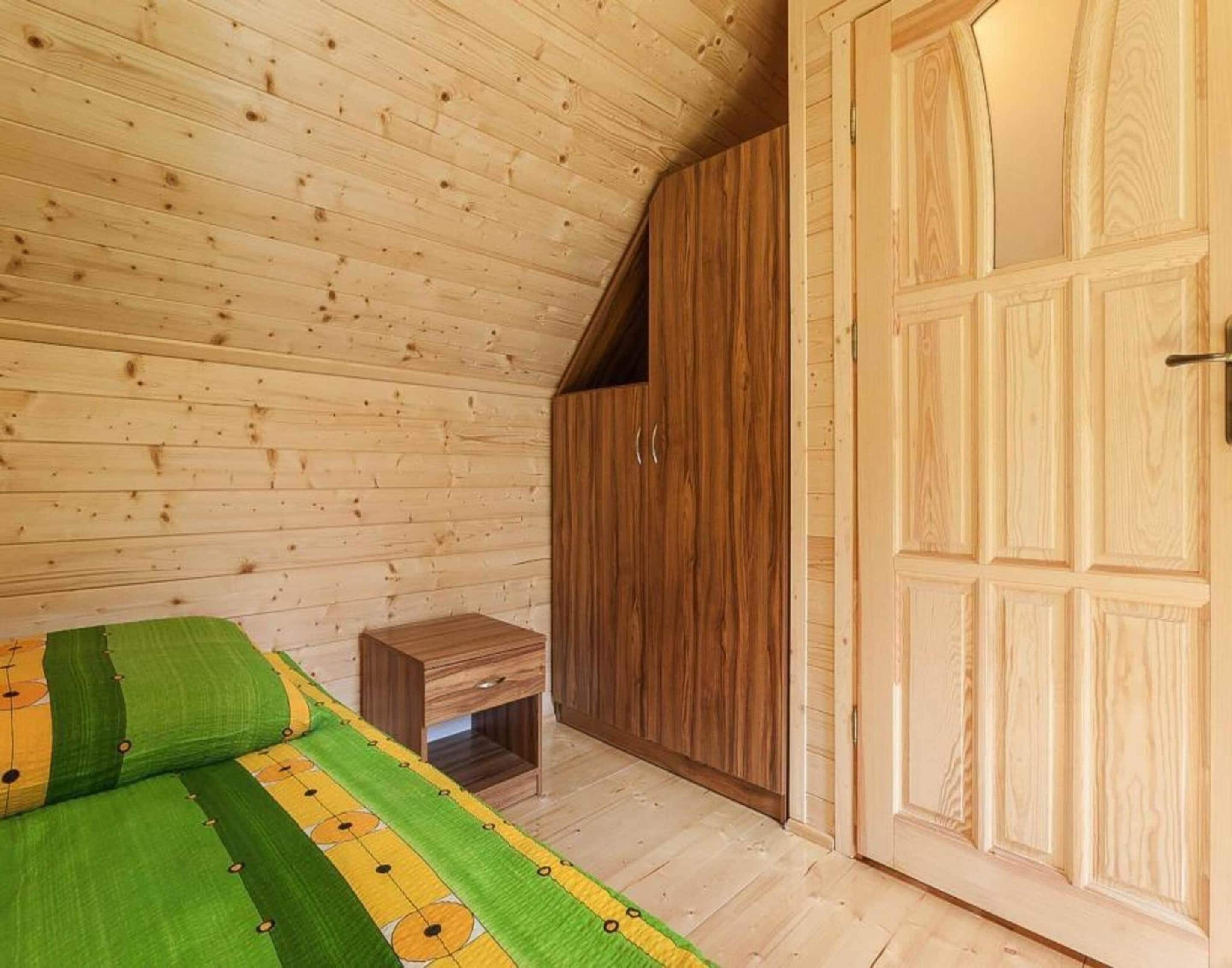 Quarto de cabana de madeira com uma cama, uma pequena mesa de madeira e um guarda-roupa.