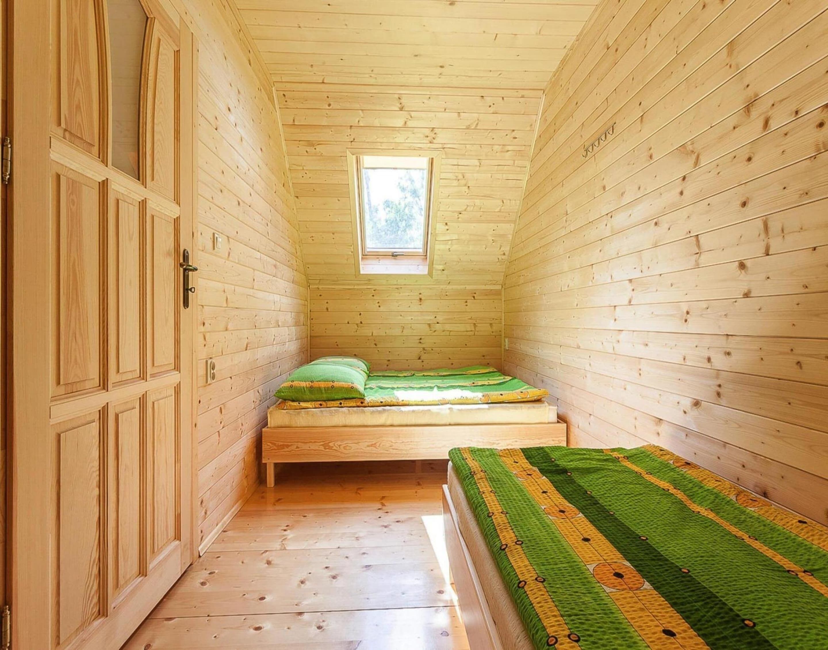 A small, single-room cabin with a wooden interior, a window, a bed, and a bench.
