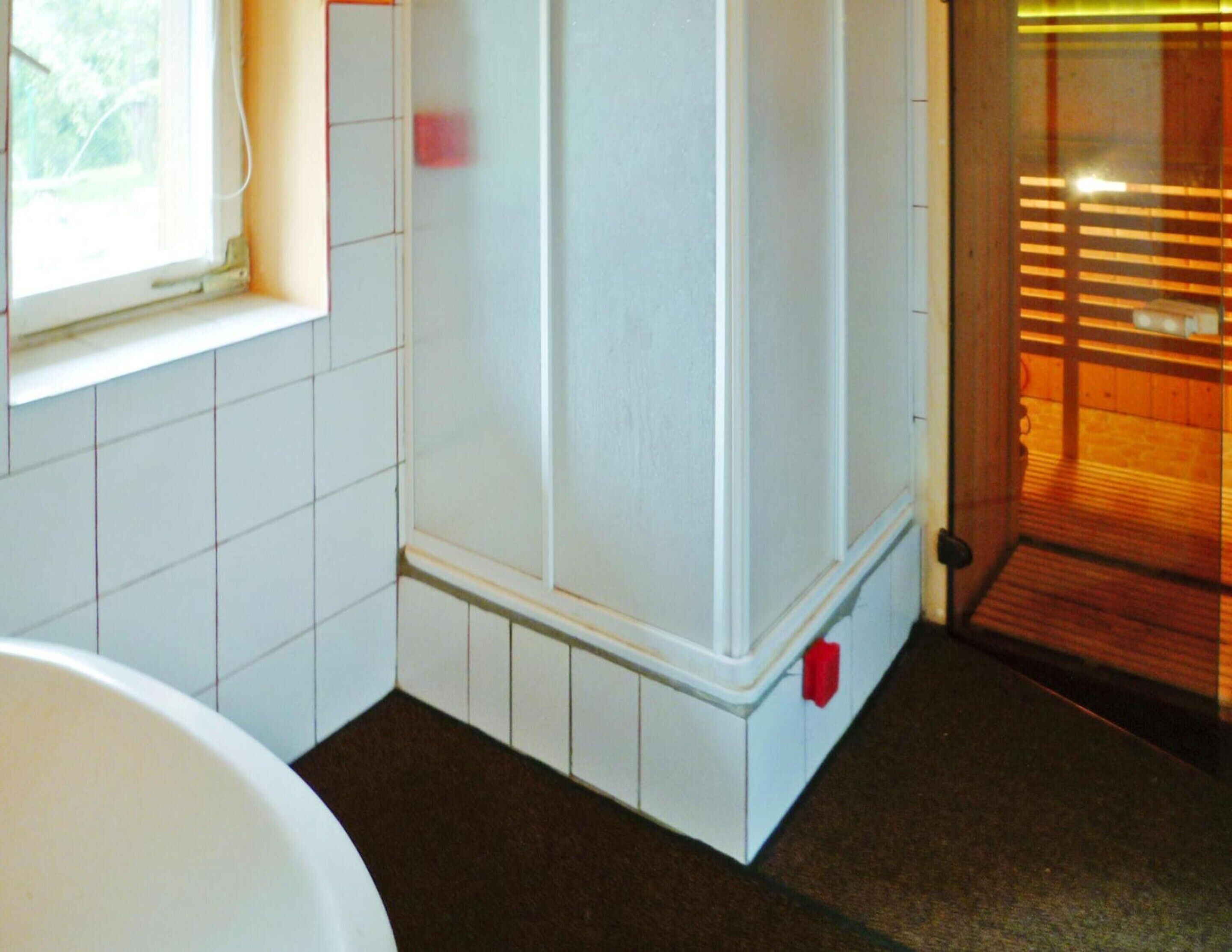 A bathroom with white tiled walls, a white bathtub, and a wooden floor.