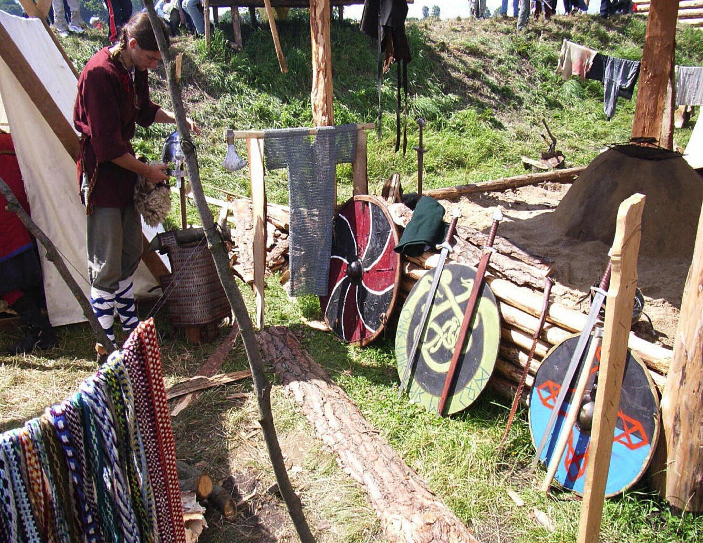 Un camping con tiendas de campaña, una mesa de madera y varios objetos, como un sombrero y un escudo.