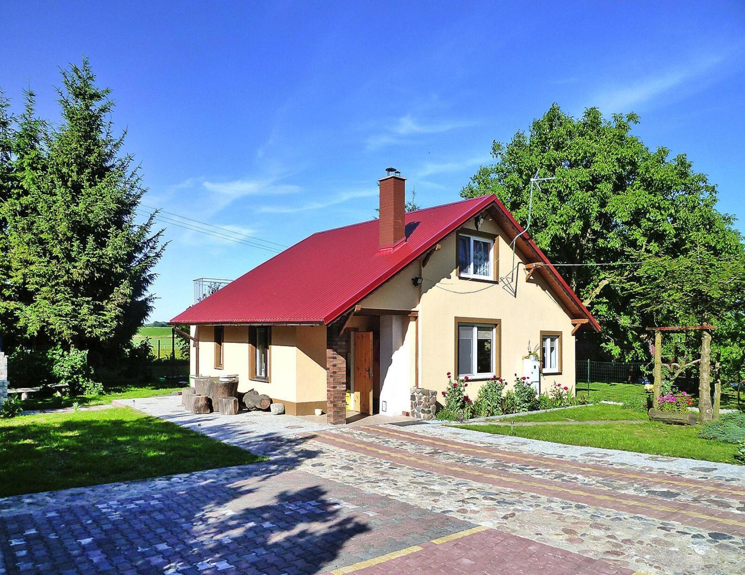 A two-story house with a red roof, beige walls, and a front porch.