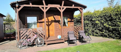 A wooden cabin with a porch, a bicycle, and two lounge chairs.