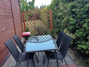 A patio with a glass-top table and four chairs, surrounded by a wooden fence and greenery. - Holiday Home in Kolczewo Near Baltic Sea (gmina Wolin)