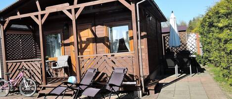 A wooden cabin with a porch, a table, and chairs.
