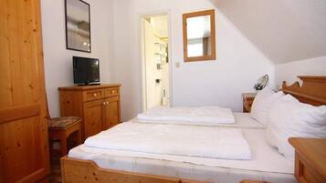 Un dormitorio con una cama de madera, un televisor sobre un mueble de madera y una puerta que da al baño.