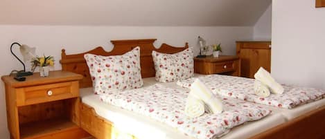 A neatly made double bed with floral bedding, wooden headboard, bedside tables with lamps, and a small potted plant.