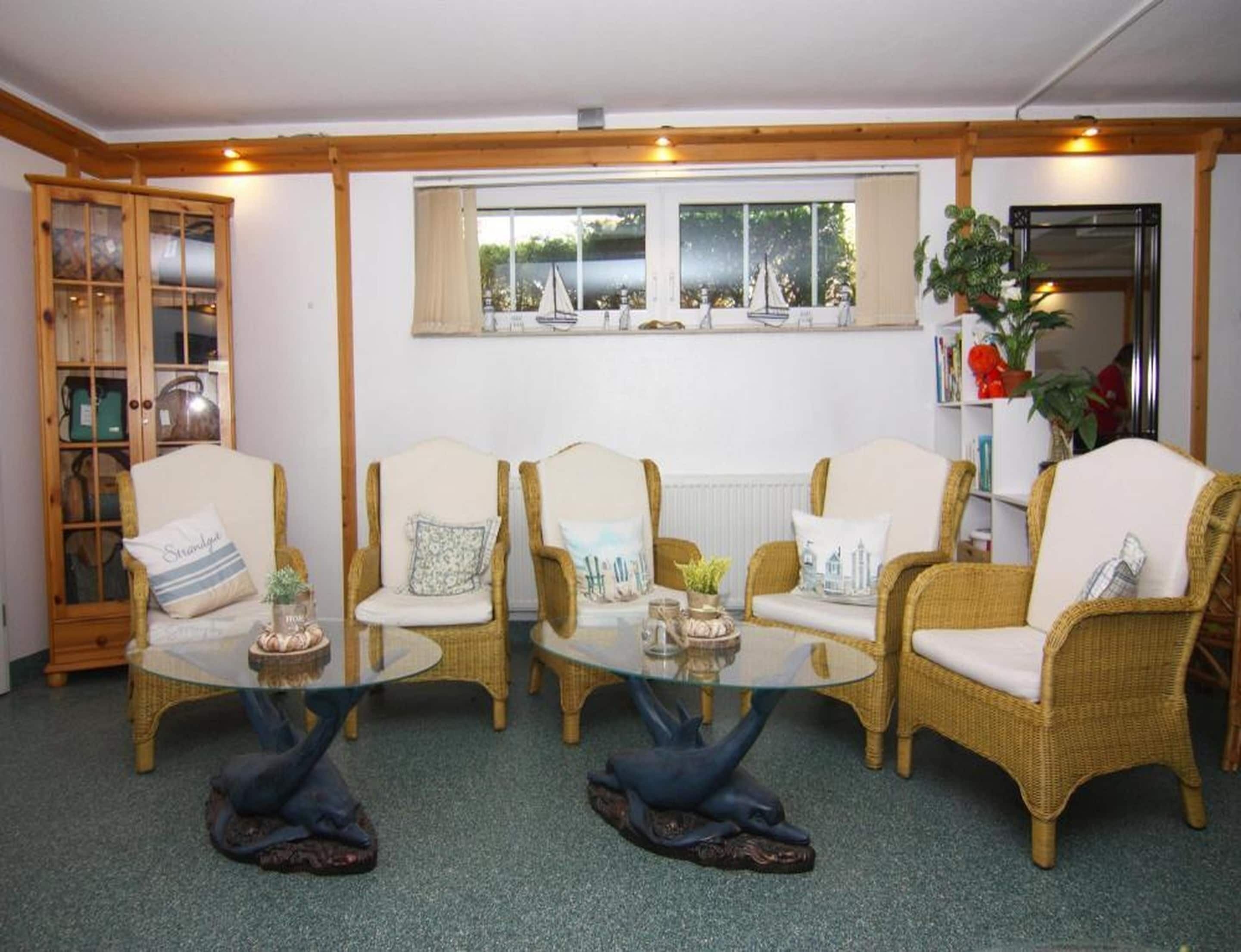 Una habitación con muebles de mimbre, una mesita de centro de vidrio y una ventana con cortinas.