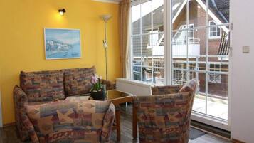 Un salón con sofás estampados, una mesa de centro, una lámpara de pie y un ventanal con vista a una casa.