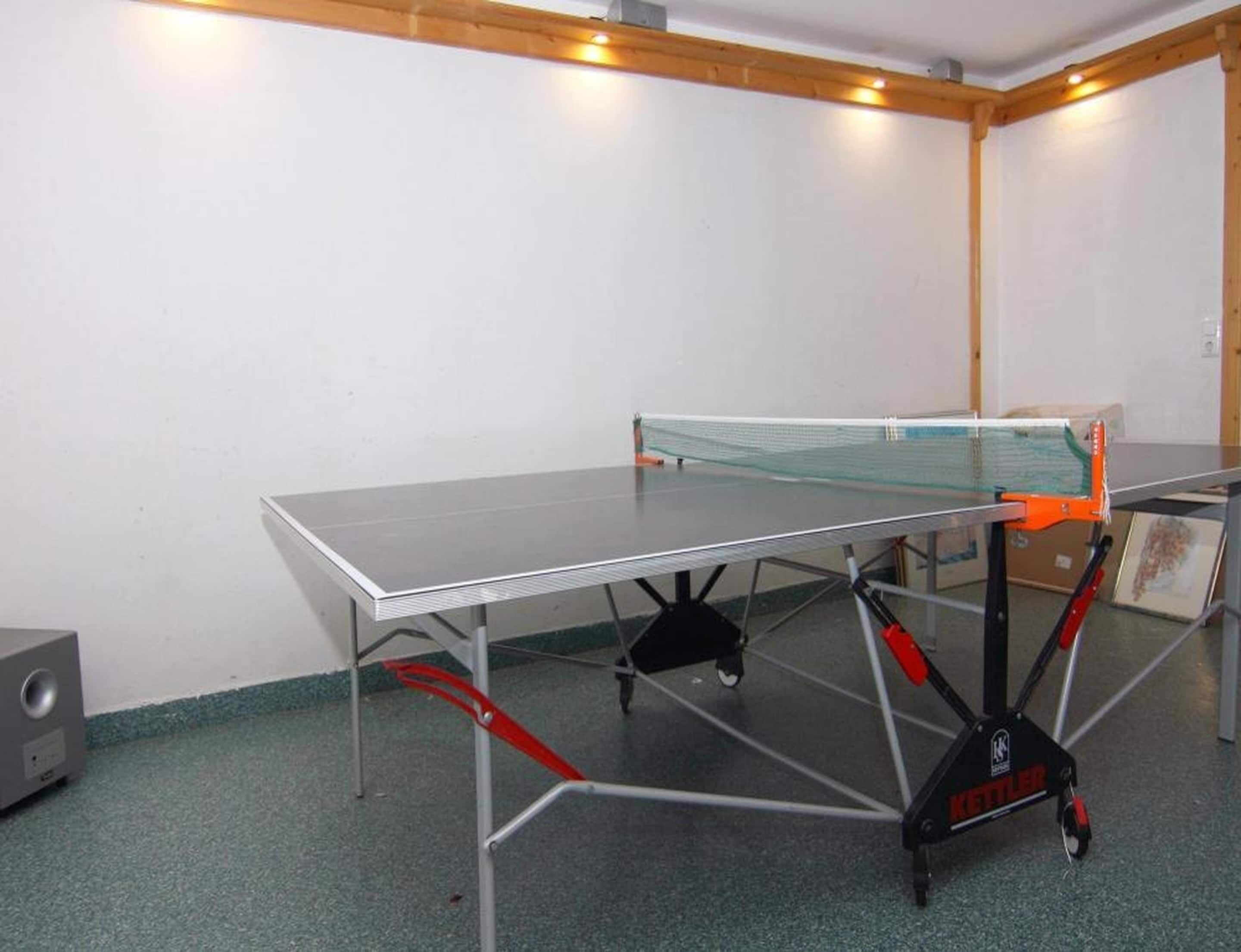 Una mesa de ping pong con red en una habitación con paredes blancas y techo de madera.