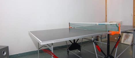 Une table de ping-pong avec un filet, dans une pièce aux murs blancs et au plafond en bois.