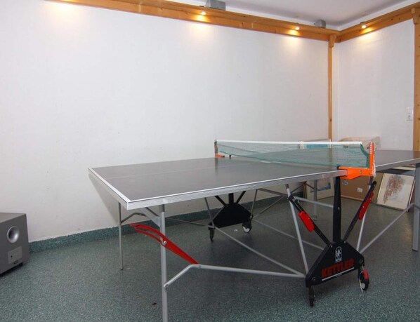 Une table de ping-pong avec un filet, dans une pièce aux murs blancs et au plafond en bois.