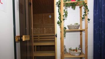 Una sala de sauna con un banco de madera y un estante con plantas y una cesta.