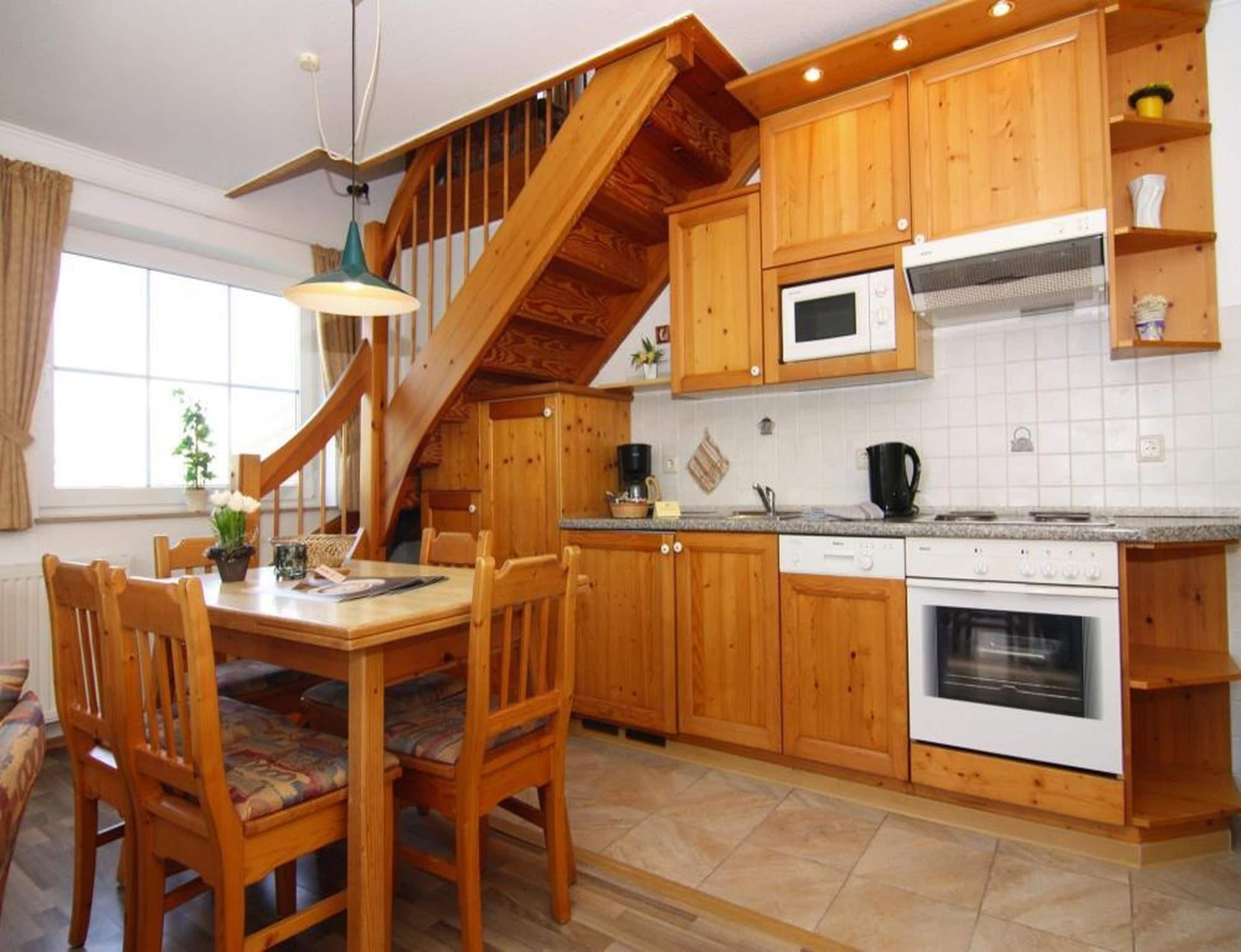 Una cocina con armarios de madera, una mesa de comedor con sillas, un microondas, un horno y una escalera.
