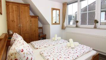 Un dormitorio con dos camas individuales, un armario de madera, una silla y una ventana con vista a un edificio.