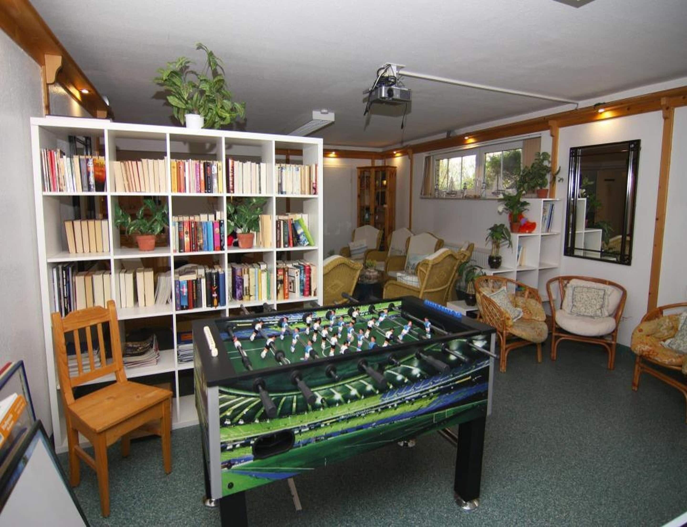 A room with a foosball table, a bookshelf, and several chairs.