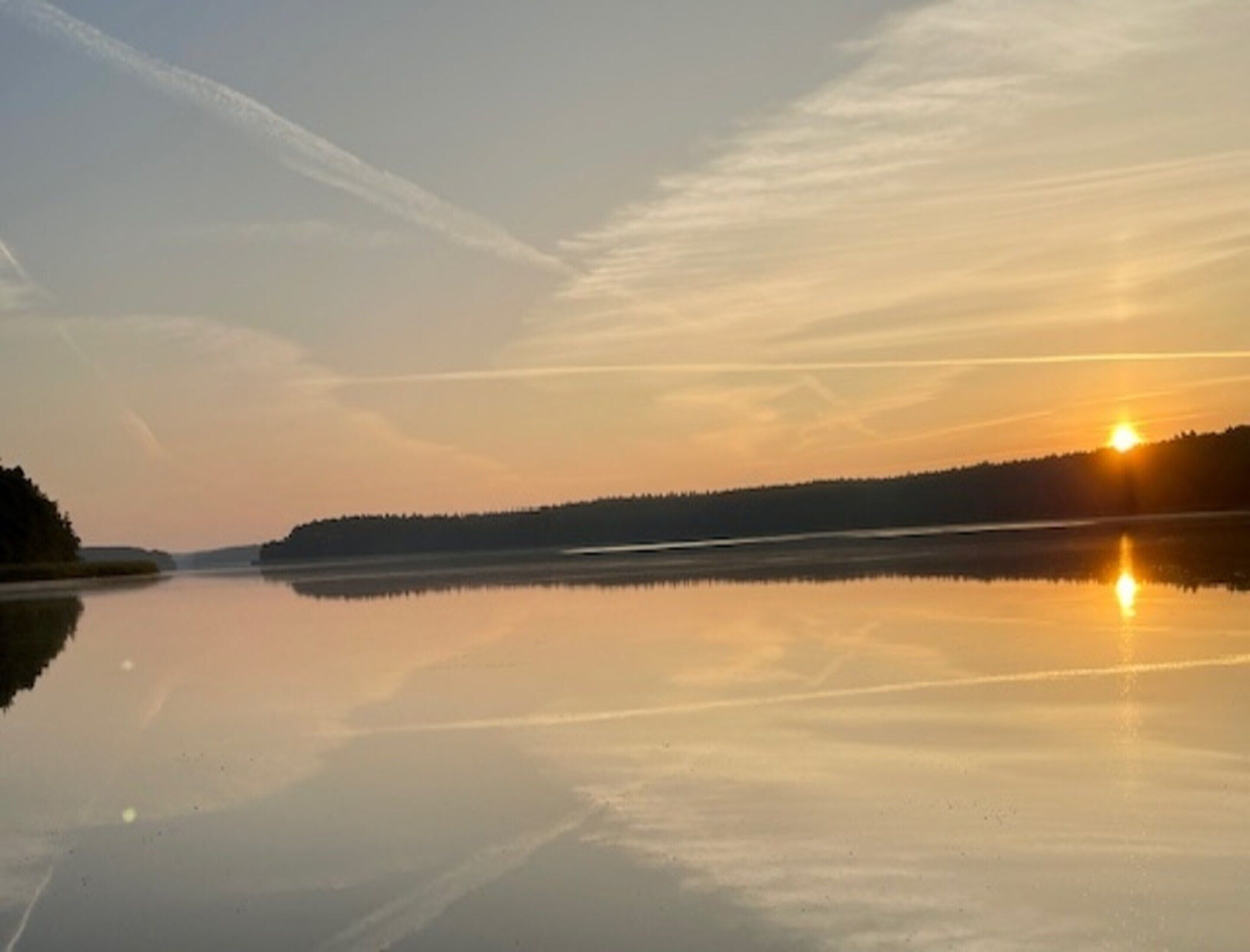 Un lago tranquilo al amanecer, con cielo despejado y árboles a lo lejos.
