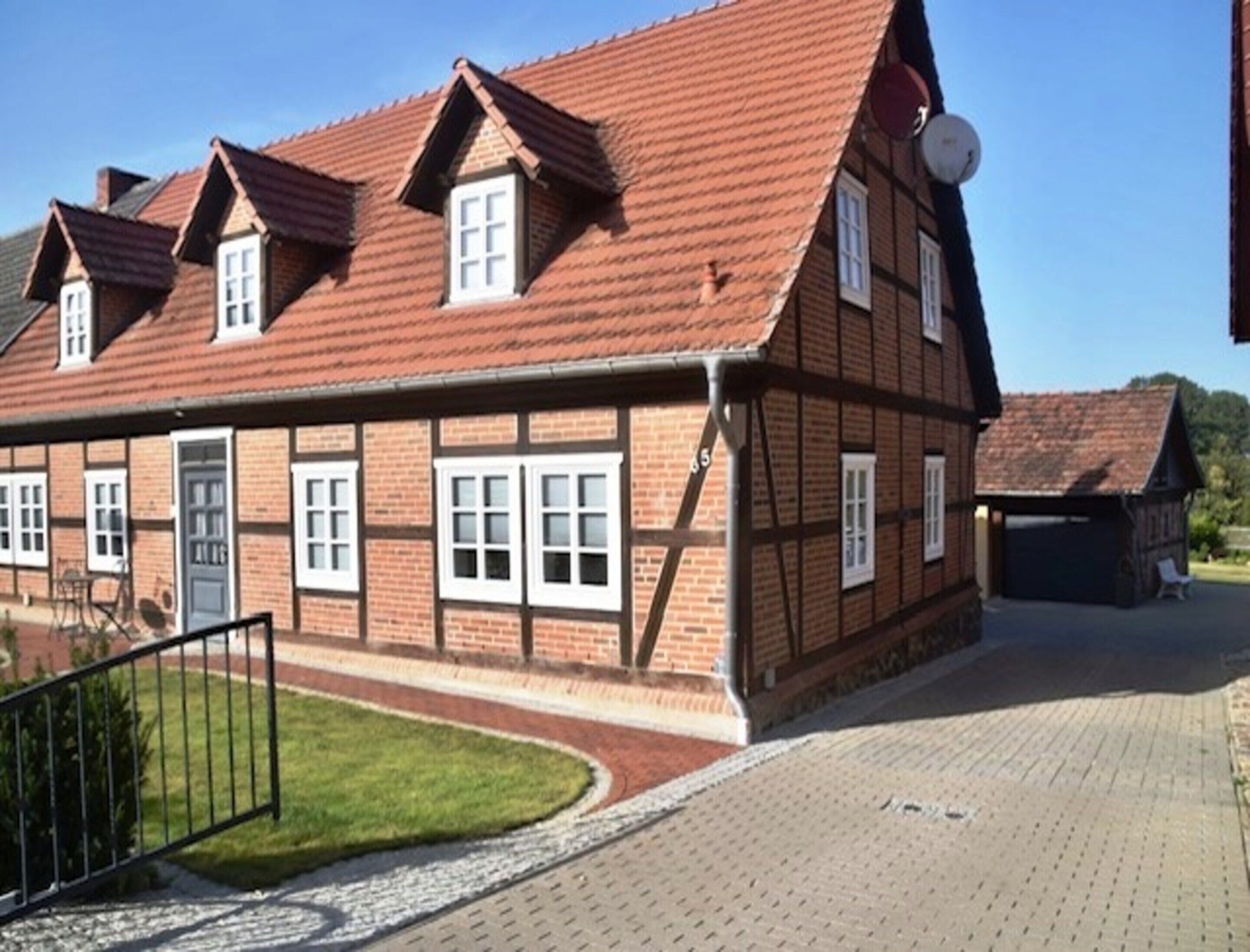 A traditional half-timbered house with a red-tiled roof, multiple windows, and a paved driveway.