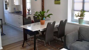 Moderni keittiö, jossa on valkoiset kaapit, ruokapöytä neljällä tuolilla ja ruukkukasvi ikkunalaudalla.