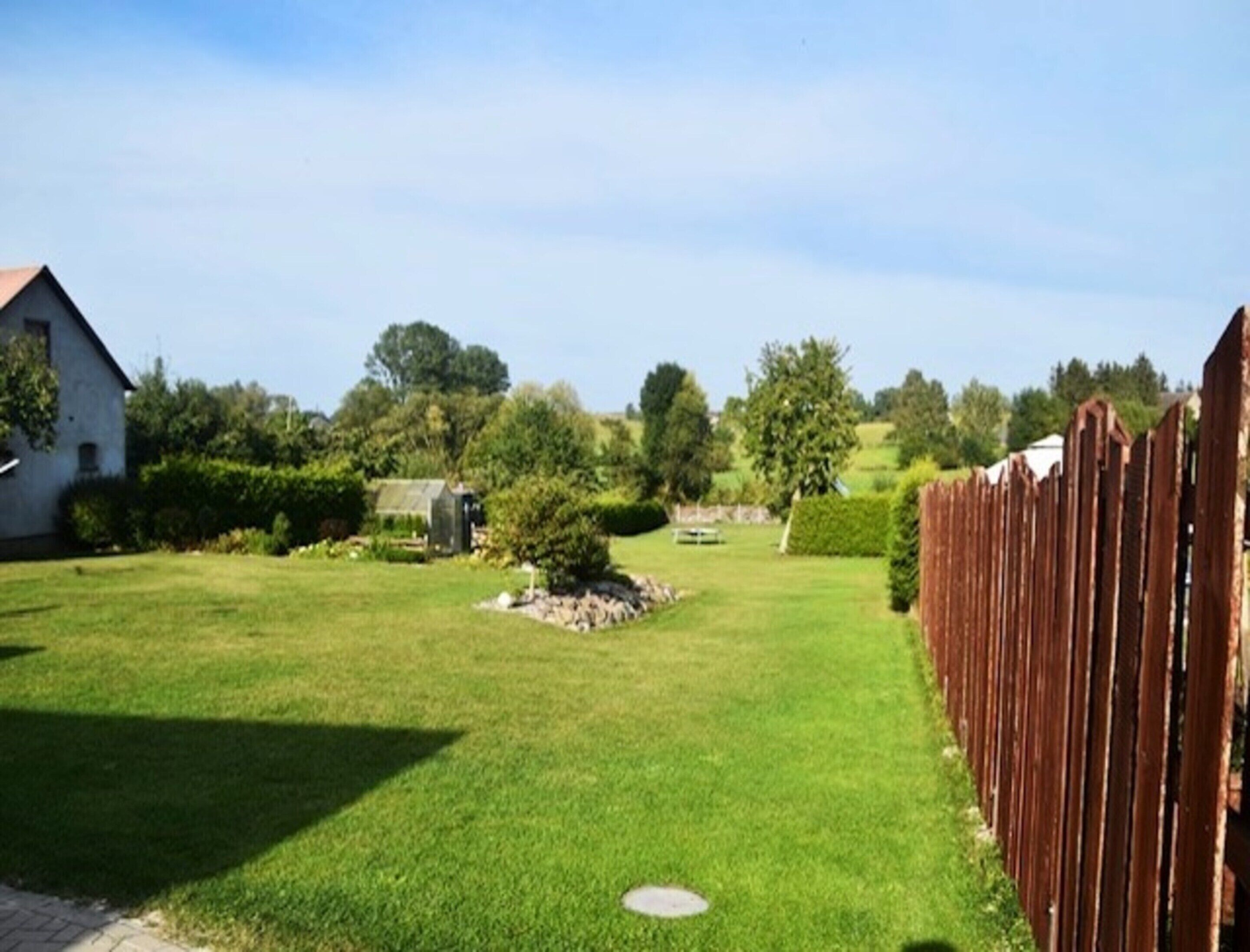 A well-maintained grassy yard with a wooden fence, a small shed, and a house in the background.
