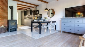 A modern kitchen with a wood-burning stove, a dining area with a table and chairs, and a grey cabinet with drawers. - Landhaus in Vollerwiek (Vollerwiek)
