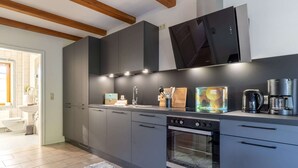 A modern kitchen with grey cabinets, a built-in oven, a coffee maker, and a window above the sink. - Landhaus in Vollerwiek (Vollerwiek)