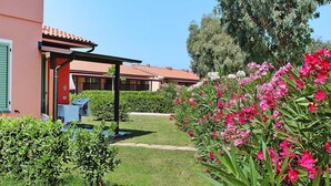 Ein Garten mit rosa Blumen, ein Gebäude mit rotem Dach und ein klarer, blauer Himmel.