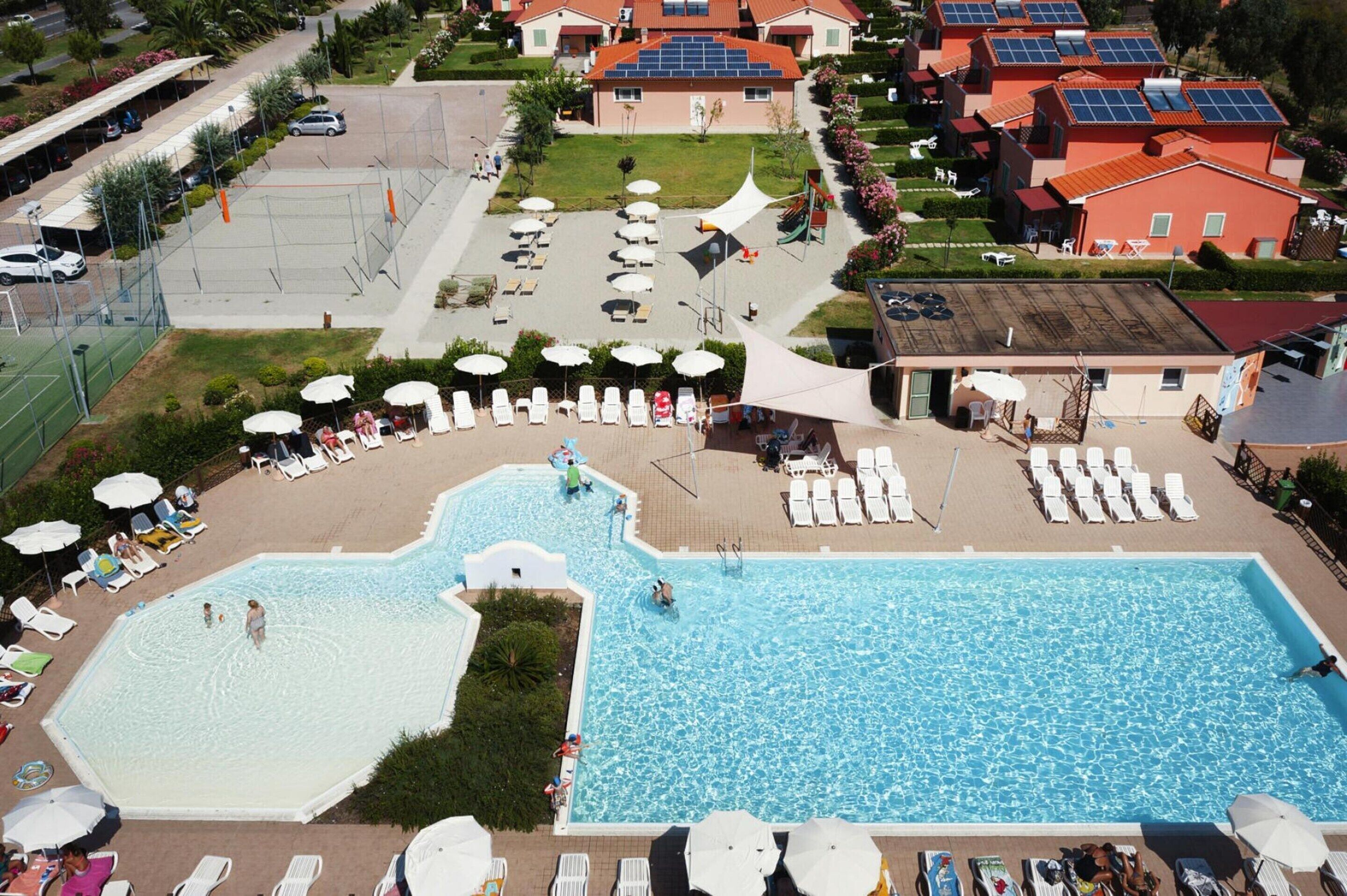 Vista aérea de un resort con una piscina grande, tumbonas y un estacionamiento.