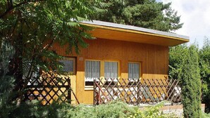 A single-story wooden house with a fenced porch, surrounded by dense greenery.