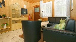 A cozy living room with a black leather sofa, a wooden cabinet with glassware, a flat-screen TV, and a fireplace.