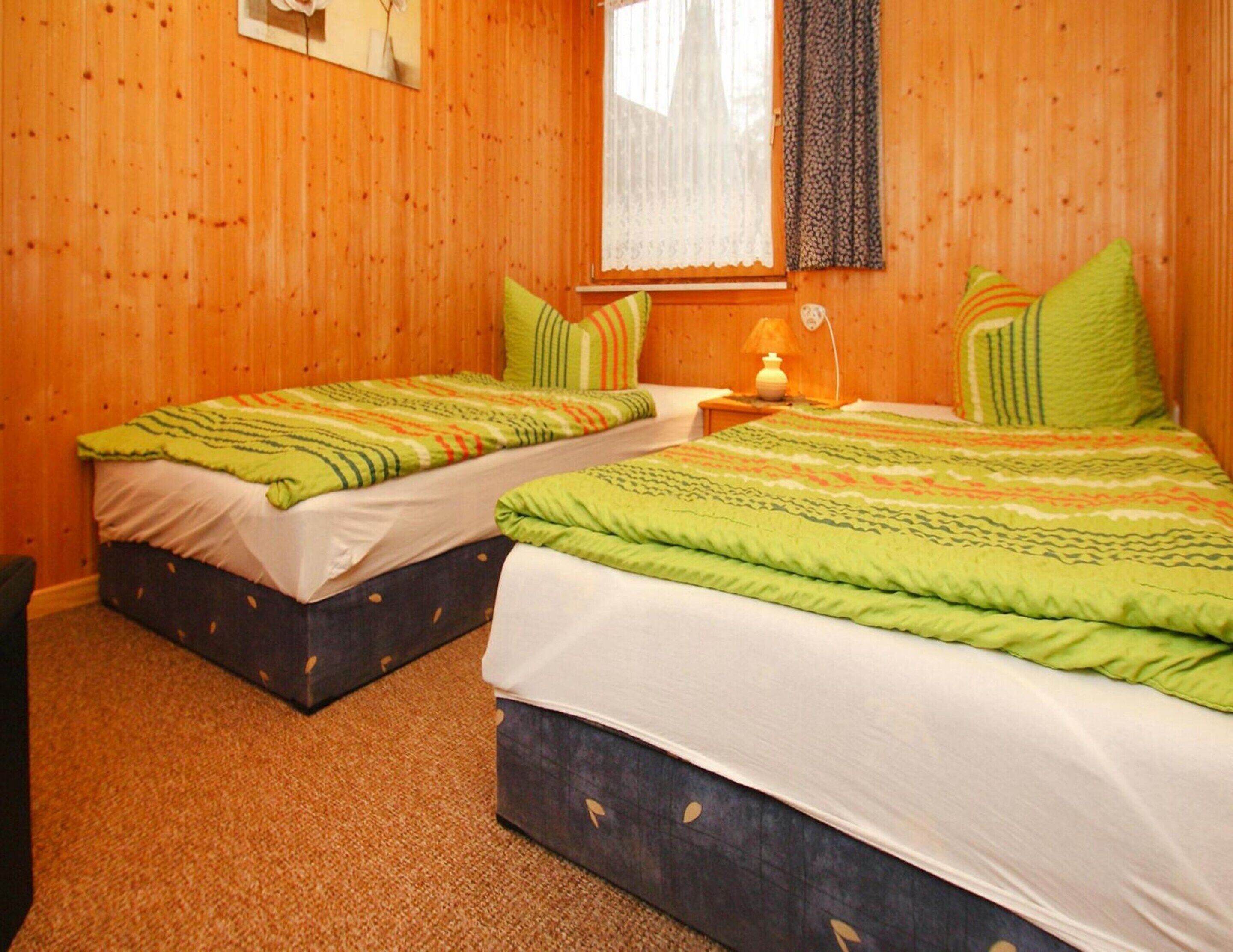 A room with two beds, each with a green and white striped bedspread, and a window with a lace curtain.