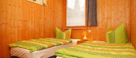 A room with two beds, each with a green and white striped bedspread, and a window with a lace curtain.