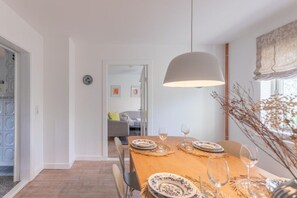 A dining area with a wooden table set for two, white walls, and a hanging light fixture. - Reetgedecktes Ferienhaus mit Kachelofen (Tetenbüll)