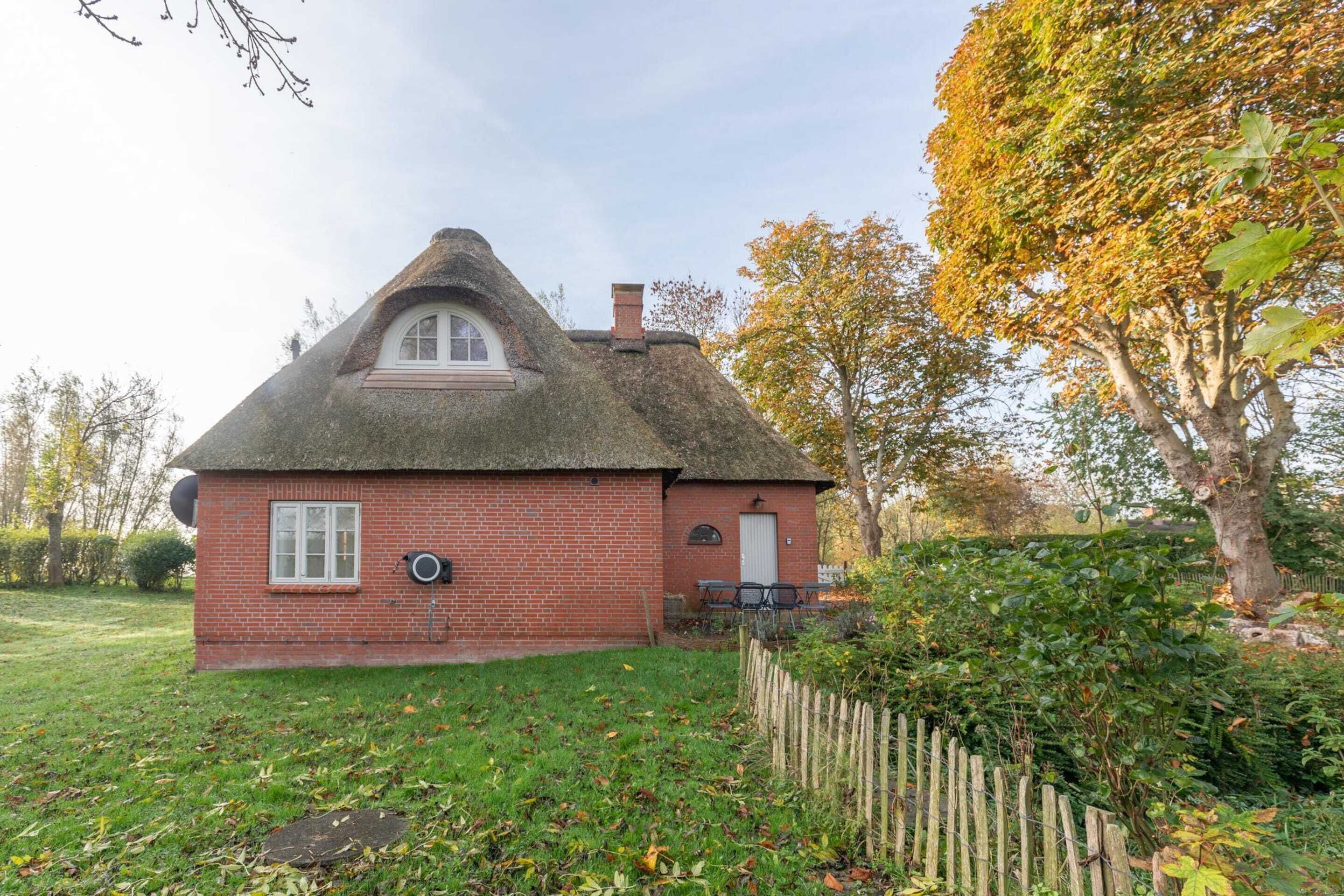 A thatched-roof house with a brick exterior, a small front porch, and a fenced yard.