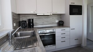 Una cocina moderna con armarios blancos, un lavamanos de acero inoxidable, una cafetera, un horno y un microondas.