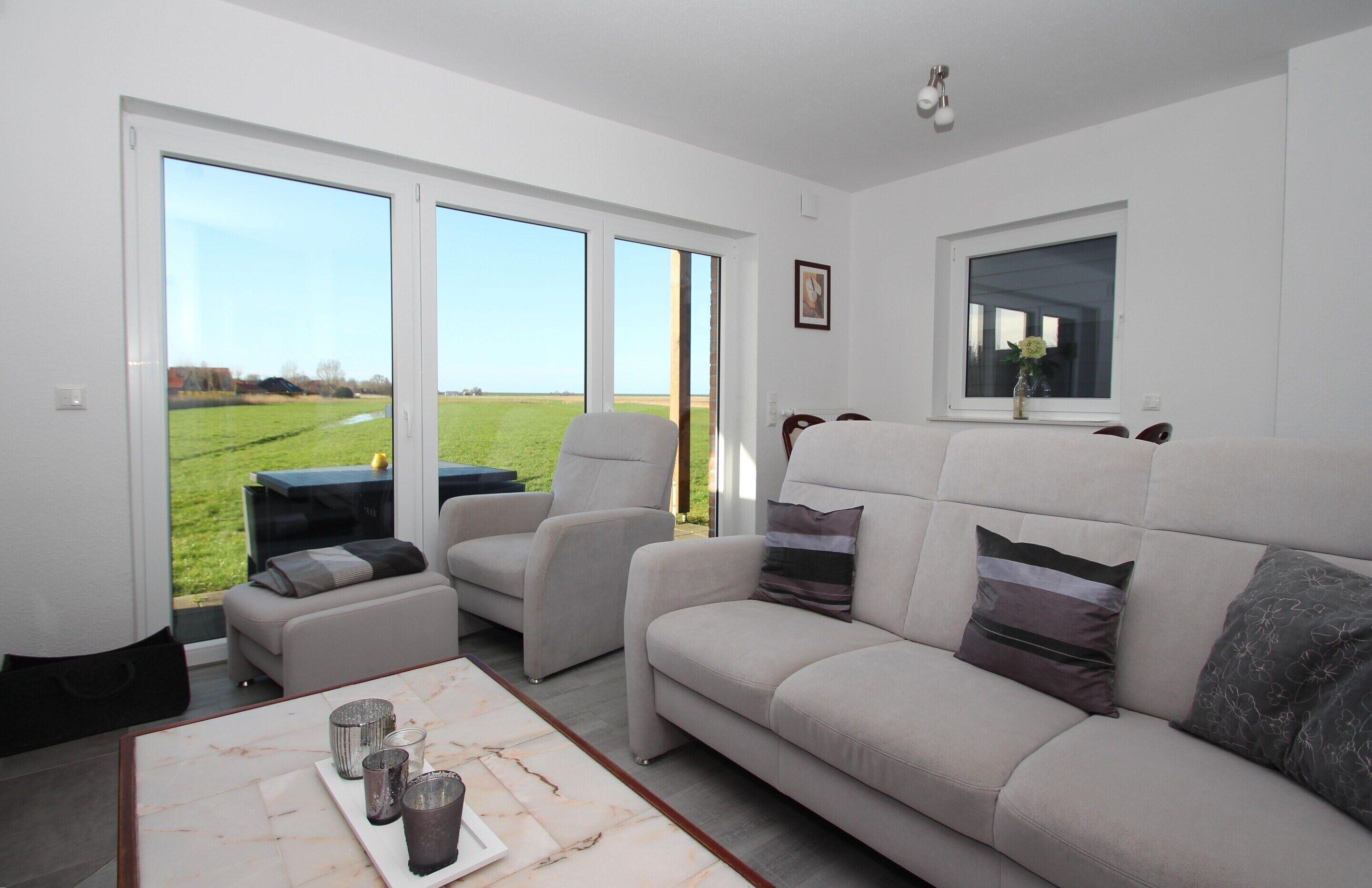 Una sala de estar moderna con un sofá, sillones y una mesa de centro. Amplias ventanas ofrecen vista a un campo verde.