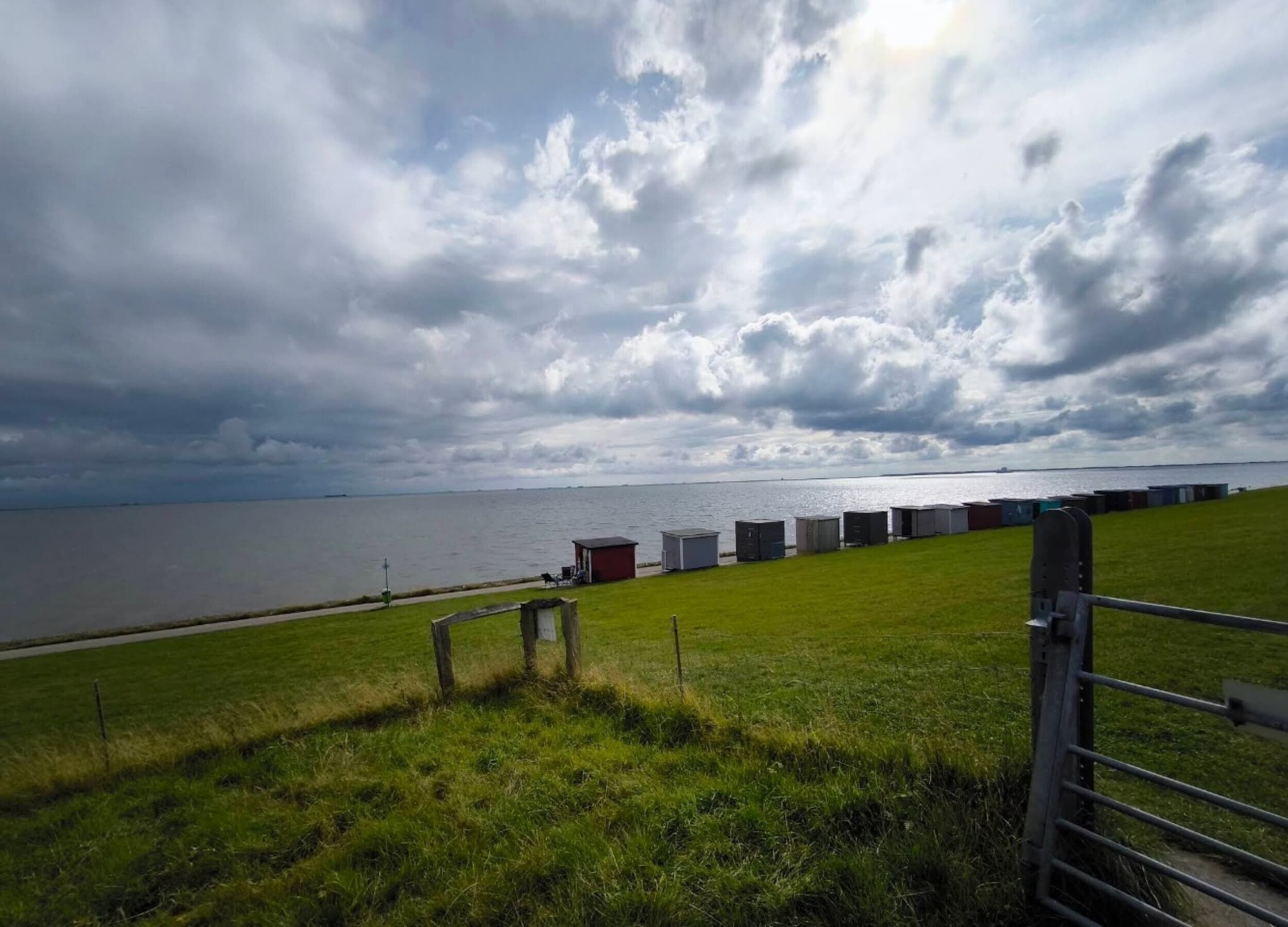 A grassy area with a metal gate, a body of water, and several shipping containers in the background.
