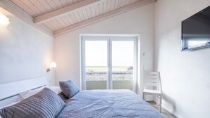 A bedroom with a bed, a chair, a TV, and a balcony with a view. - Luxurios Eingerichtetes Ferienhaus in Strandnahe (Dagebuell)