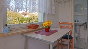 A small kitchen with a table, chairs, a microwave, and a window with lace curtains. - Gemutlicher Bungalow in Freest (Kröslin)